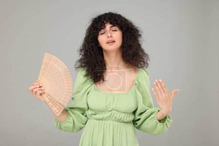 Woman with hand fan suffering from heat on light grey background