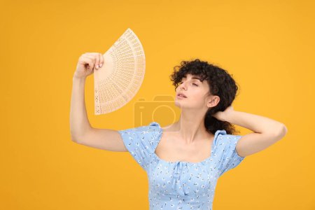 Woman with hand fan suffering from heat on orange background