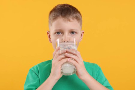 Téléchargez les photos : Mignon garçon boire du lait frais à partir de verre sur fond orange - en image libre de droit