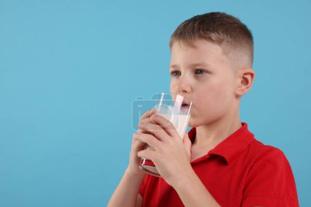 Téléchargez les photos : Mignon garçon boire du lait frais à partir de verre sur fond bleu clair, espace pour le texte - en image libre de droit