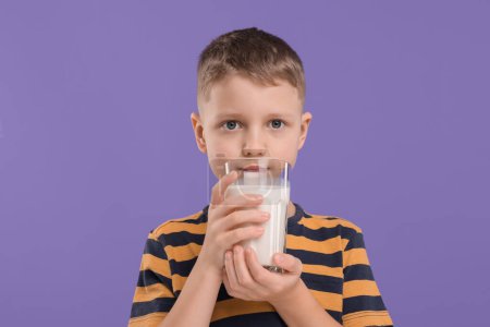 Téléchargez les photos : Mignon garçon avec un verre de lait frais sur fond violet - en image libre de droit