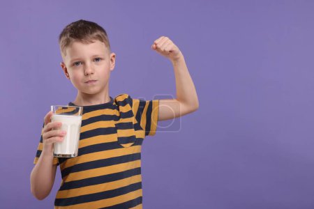 Téléchargez les photos : Garçon mignon avec un verre de lait frais montrant sa force sur fond violet, espace pour le texte - en image libre de droit