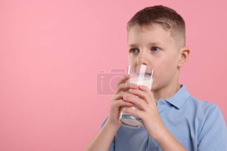 Téléchargez les photos : Mignon garçon boire du lait frais à partir de verre sur fond rose, espace pour le texte - en image libre de droit