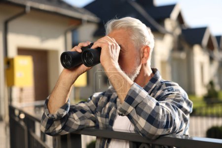 Téléchargez les photos : Concept de vie privée. Homme âgé curieux avec des jumelles espionnant les voisins au-dessus de la clôture à l'extérieur - en image libre de droit