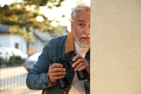 Konzept des Privatlebens. Neugieriger Senior mit Fernglas spioniert Nachbarn im Freien aus