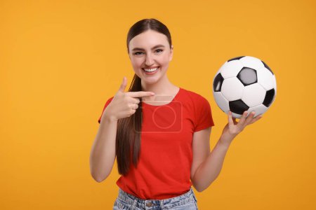 Photo for Happy soccer fan pointing at ball on orange background - Royalty Free Image