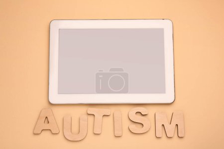 Téléchargez les photos : Word Autisme en lettres de bois et tablette sur fond beige, pose plate - en image libre de droit