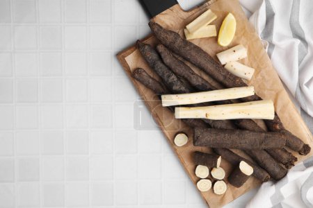 Raw salsify roots and lemon on white tiled table, top view. Space for text