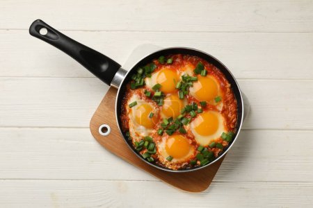 Delicious shakshuka in frying pan on white wooden table, top view