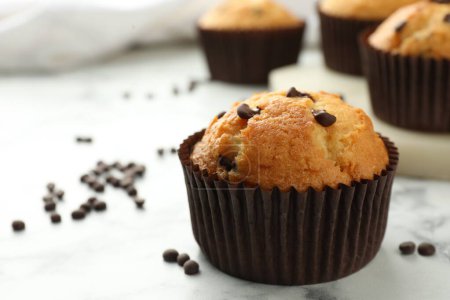 Photo for Delicious sweet muffin with chocolate chips on white marble table, closeup. Space for text - Royalty Free Image