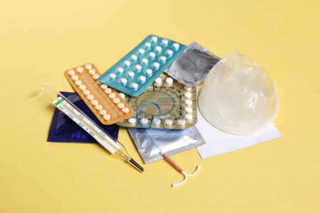 Contraceptive pills, condoms, intrauterine device and thermometer on yellow background. Different birth control methods