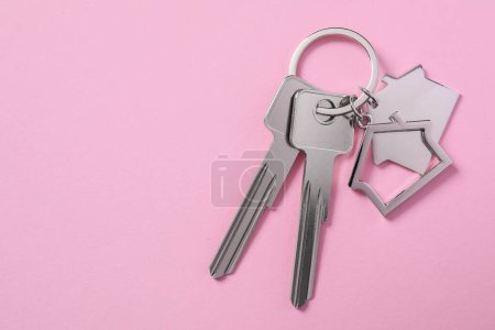 Metallic keys with keychains in shape of houses on pink background, top view. Space for text