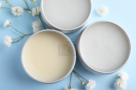 Different lip balms and gypsophila on light blue background, flat lay