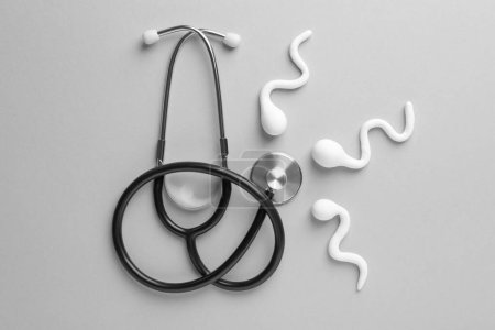 Reproduktionsmedizin. Figuren von Spermien und Stethoskop auf grauem Hintergrund, flach gelegt