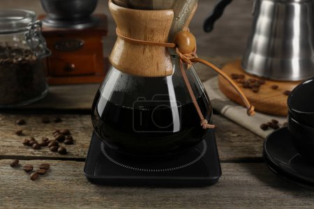 Glas-Chemex-Kaffeemaschine mit Kaffee und Bohnen auf Holztisch, Nahaufnahme
