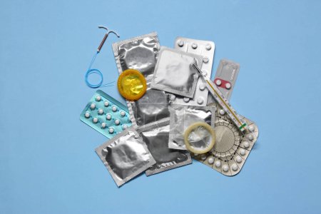 Contraceptive pills, condoms, intrauterine device and thermometer on light blue background, flat lay. Different birth control methods