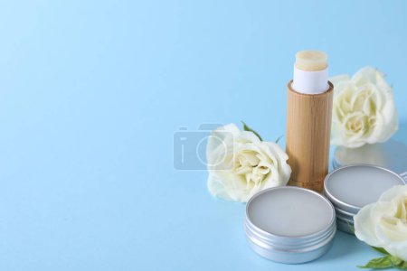 Different lip balms and rose flowers on light blue background. Space for text