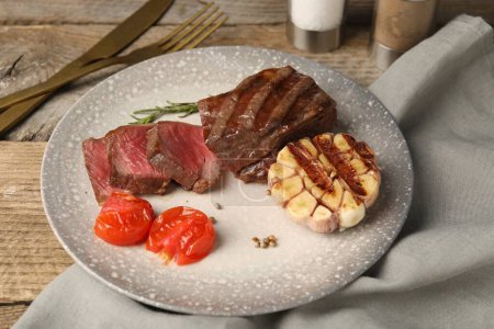 Delicious grilled beef steak with spices and tomatoes on wooden table