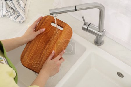 Woman washing wooden cutting board at sink in kitchen, closeup