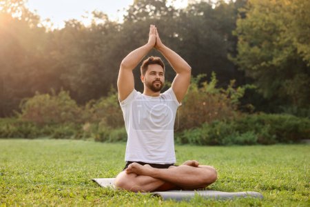 Téléchargez les photos : Homme pratiquant le yoga sur tapis à l'extérieur. Pose de lotus - en image libre de droit