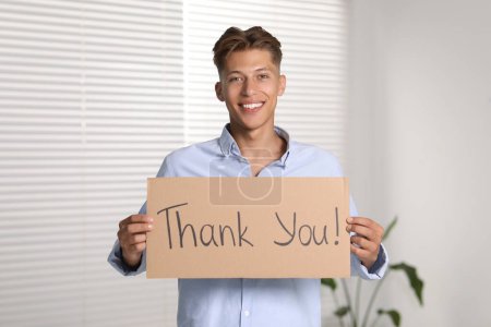 Hombre feliz sosteniendo hoja de cartón con frase Gracias en el interior