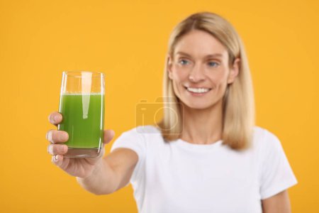 Happy woman with glass of fresh celery juice on orange background, selective focus