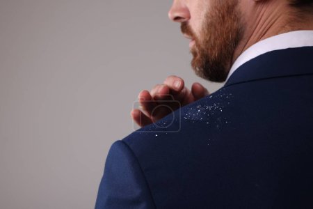 Man swiping dandruff of his suit against grey background, closeup. Space for text