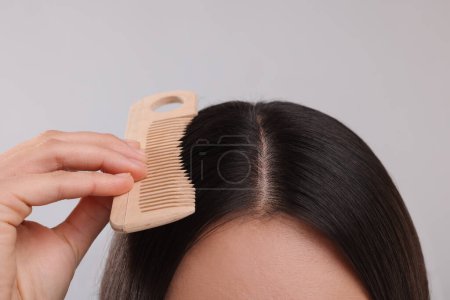 Téléchargez les photos : Femme avec peigne examinant ses cheveux et son cuir chevelu sur fond gris, gros plan - en image libre de droit