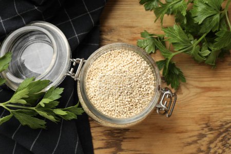 Photo for Dry quinoa seeds in glass jar and parsley on wooden table, top view - Royalty Free Image