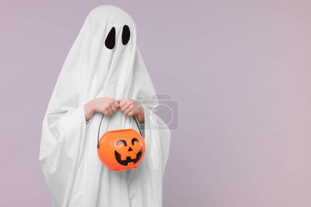 Foto de Niño en traje de fantasma blanco sosteniendo cubo de calabaza sobre fondo gris claro, espacio para el texto. Halloween celebración - Imagen libre de derechos