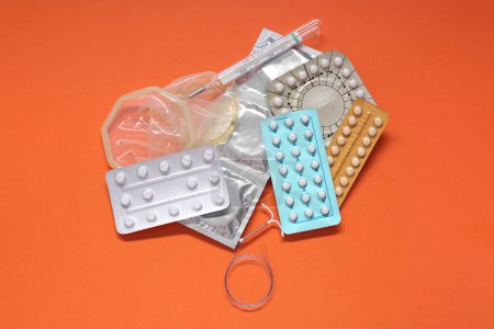 Contraceptive pills, condoms, intrauterine device and thermometer on orange background, flat lay. Different birth control methods