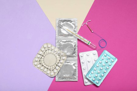 Contraceptive pills, condoms, intrauterine device and thermometer on color background, flat lay. Choice of birth control method