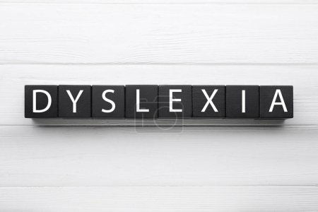 Black cubes with word Dyslexia on white wooden background, flat lay