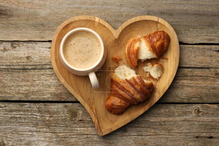 Delicious fresh croissant and cup of coffee on wooden table, top view