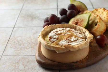 Lecker gebackener Brie-Käse und Produkte auf hellem Kacheltisch, Nahaufnahme. Raum für Text