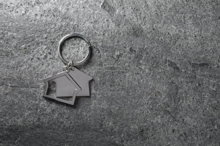 Metal keychain in shape of houses on grey textured table, top view. Space for text