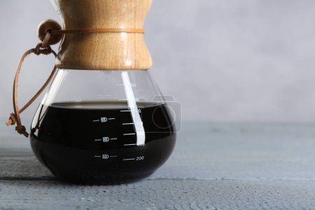 Glass chemex coffeemaker with tasty drip coffee on grey wooden table, closeup. Space for text