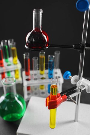Retort stand and laboratory glassware with liquids on table against black background, closeup