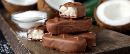 Delicious milk chocolate candy bars with coconut filling on wooden board, closeup. Banner design