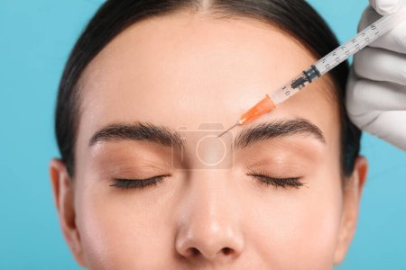 Médecin faisant une injection faciale à une jeune femme sur fond bleu clair, gros plan. Chirurgie esthétique