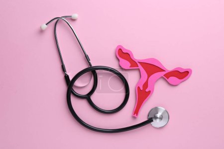 Reproductive medicine. Paper uterus and stethoscope on pink background, top view