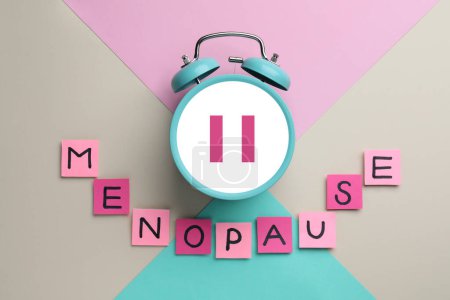Menopausia palabra de notas adhesivas con letras y despertador con símbolo de pausa en el fondo de color, vista superior