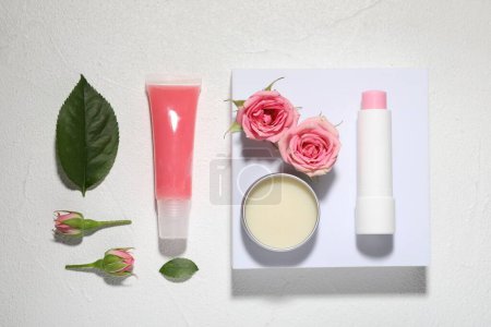 Flat lay composition with lip balms and rose flowers on white textured background