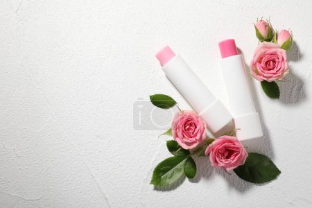 Lip balms and rose flowers on white textured background, flat lay. Space for text