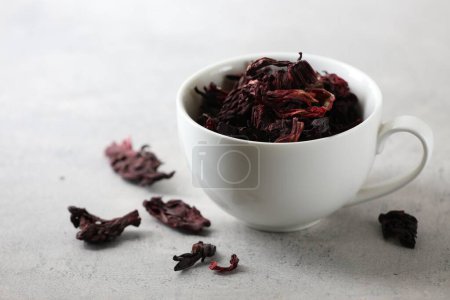 Aromatic hibiscus tea. Dried roselle calyces in cup on light table, closeup and space for text