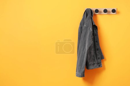 Photo for Rack with dark gray denim jacket on orange wall, space for text - Royalty Free Image
