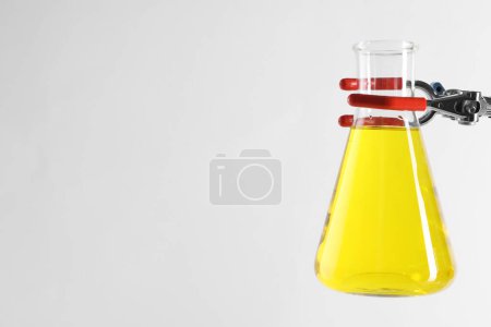 Retort stand and laboratory flask with liquid on white background, closeup. Space for text