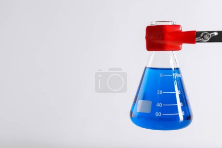 Retort stand and laboratory flask with liquid on white background, closeup. Space for text