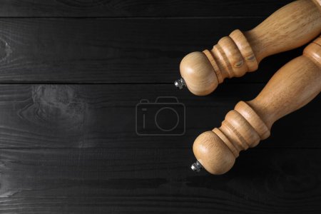 Salt and pepper shakers on black wooden table, flat lay. Space for text