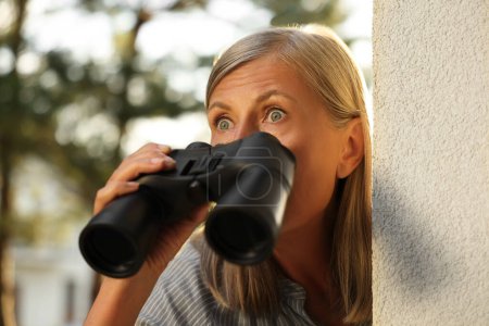 Konzept des Privatlebens. Neugierige Seniorin mit Fernglas spioniert Nachbarn im Freien aus